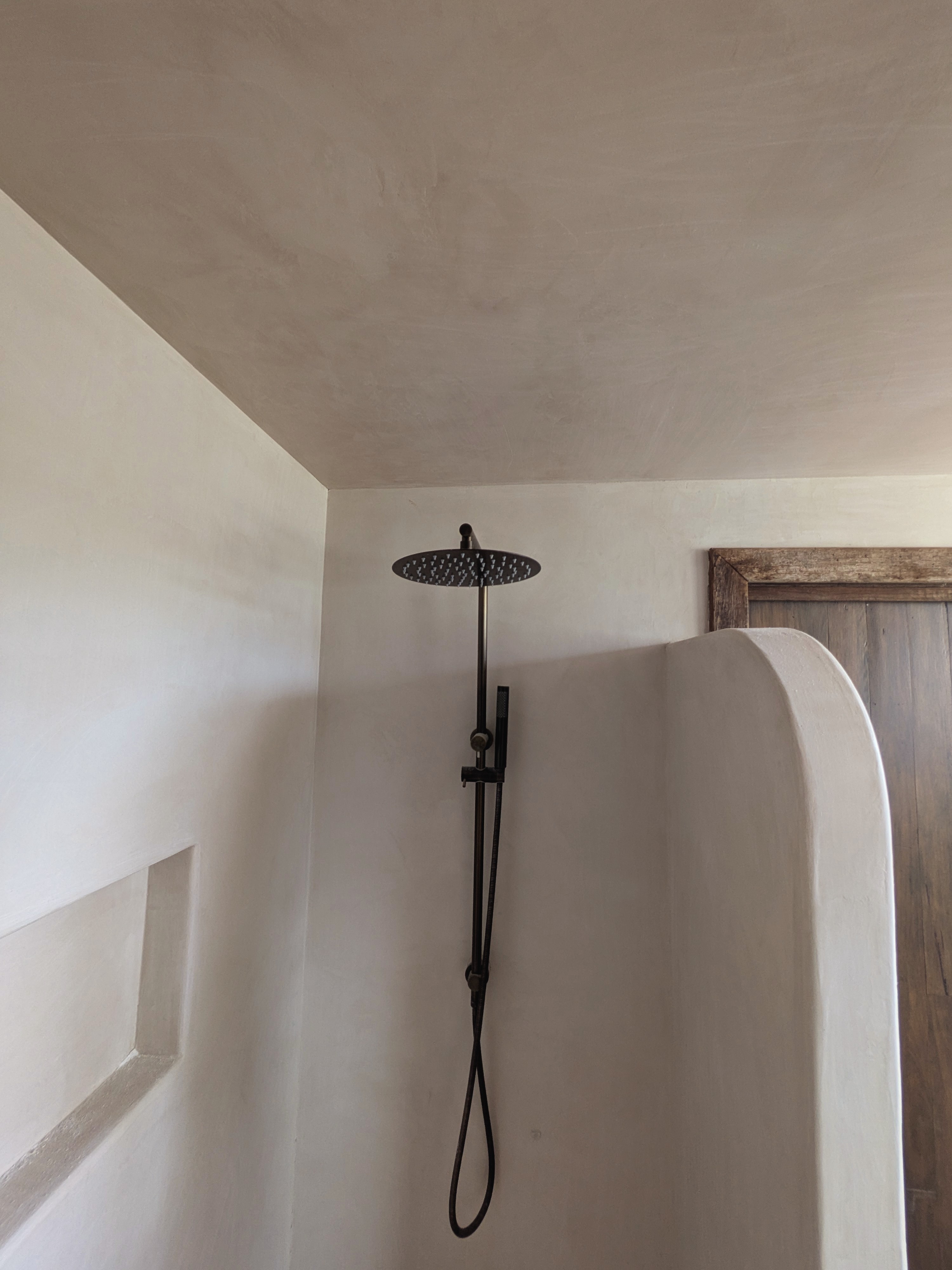 Modern microcement bathroom shower with seamless light grey walls, black rainfall showerhead, and minimalist black fixtures